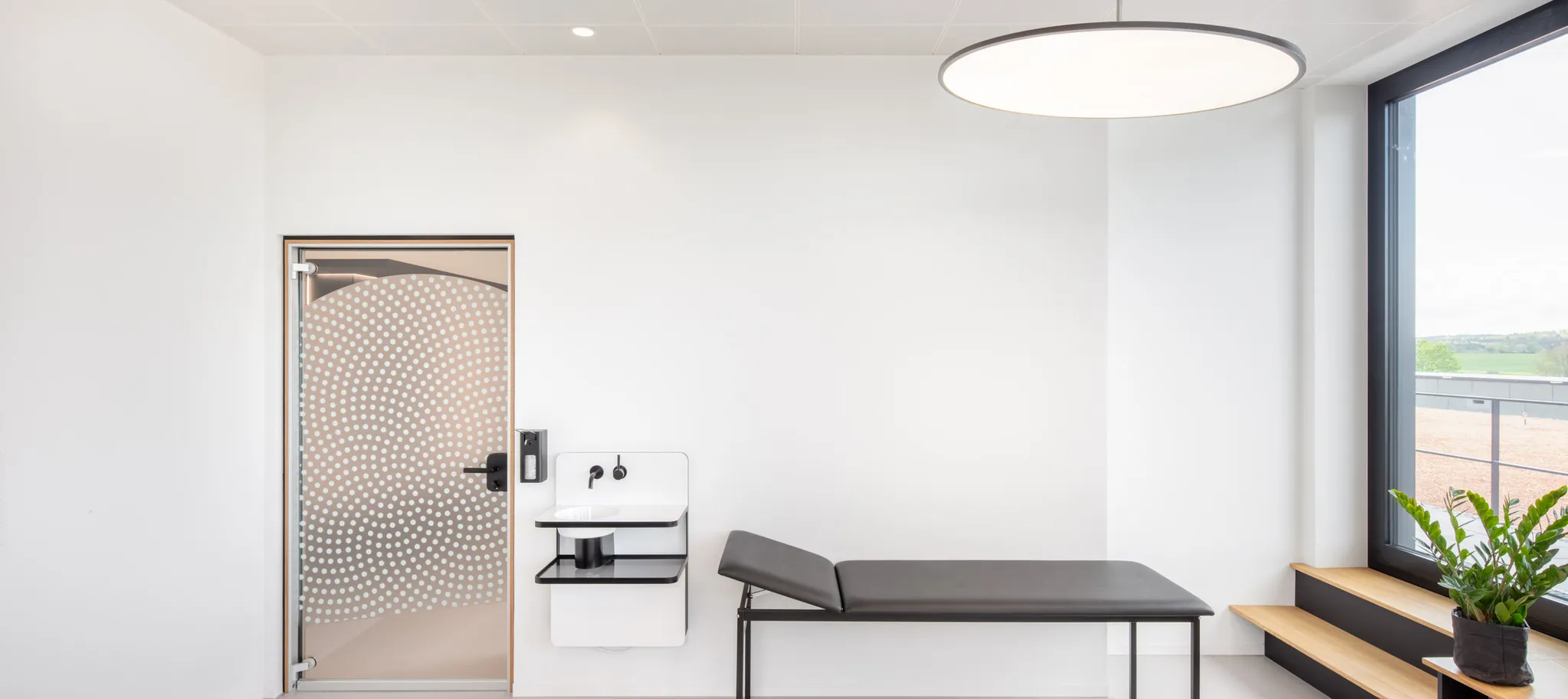 wineo PURLINE Bioboden Modernes Behandlungszimmer mit großen Fenstern und einer medizinischen Liege auf grauem Betonboden